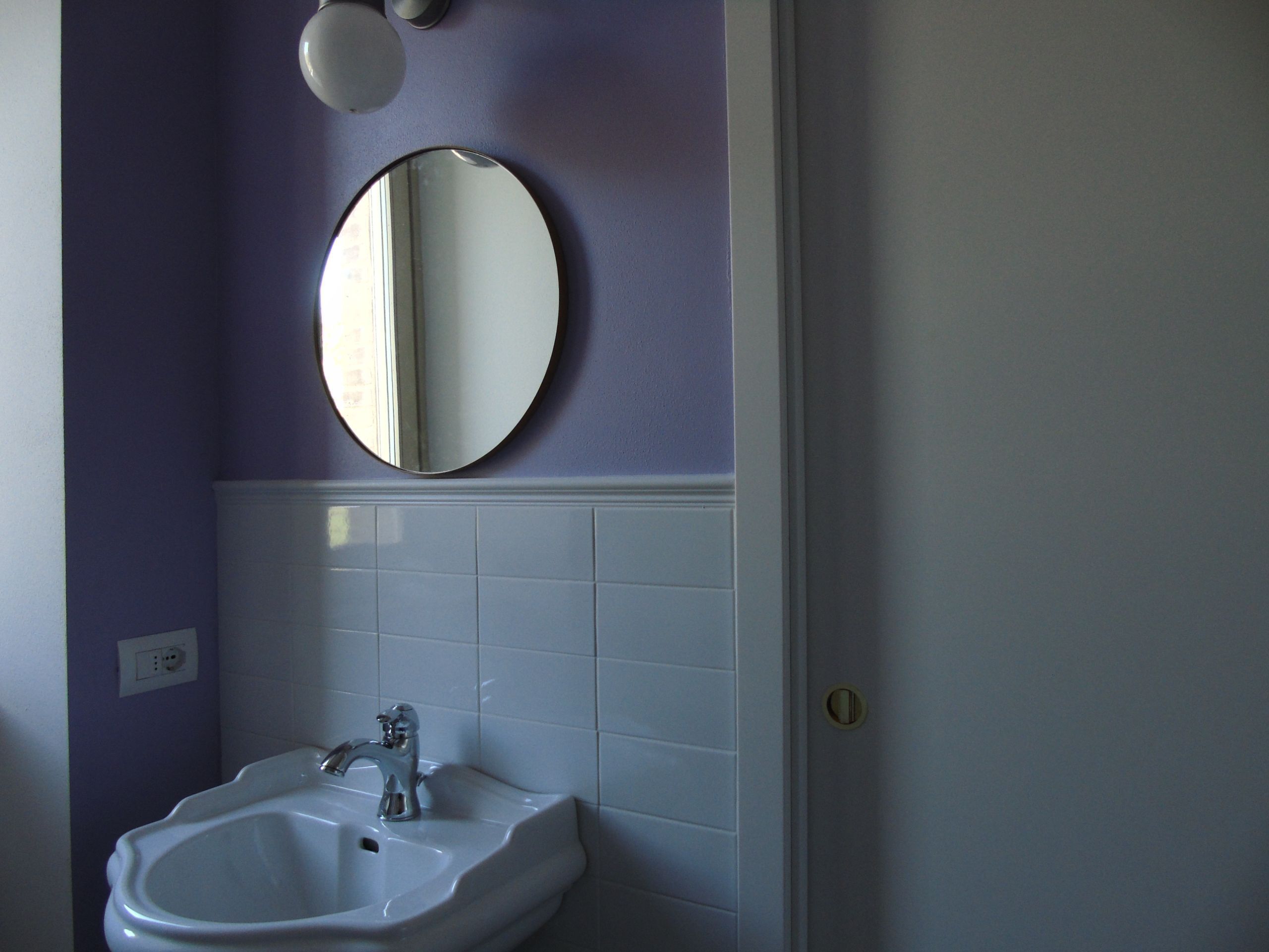 A bathroom with a white sink, a round mirror, and a light fixture above the mirror.
