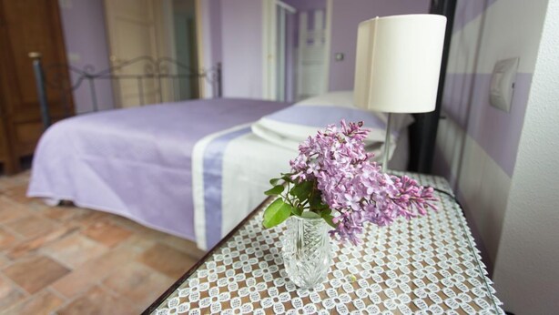 Ein Schlafzimmer mit einem Bett, einem Nachttisch mit Blumen in einer Vase und einer Lampe.
