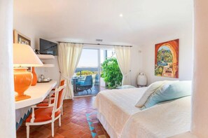A hotel room with a bed, a desk with a lamp, a TV, and a balcony with a table and chairs. - HOTEL MARINA DI CAVU BONIFACIO (Bonifacio)