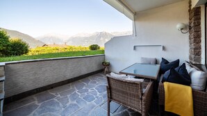 A balcony with a stone floor, wicker furniture, a glass table, and a view of mountains.