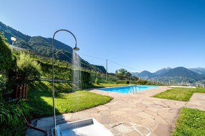 A swimming pool with a showerhead, surrounded by a stone patio, with mountains in the background. - Apartment 'Ella' with Mountain View, Pool (June - August), Private Terrace and Wi-Fi (Merano)