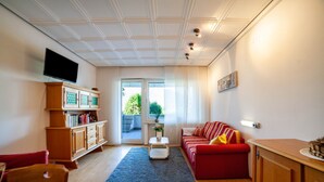 A living room with a red sofa, wooden cabinet, flat-screen TV, and a small table with a vase.