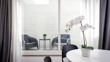 Quarto moderno com uma grande janela, uma mesa redonda, duas cadeiras e uma orquídea em vaso.