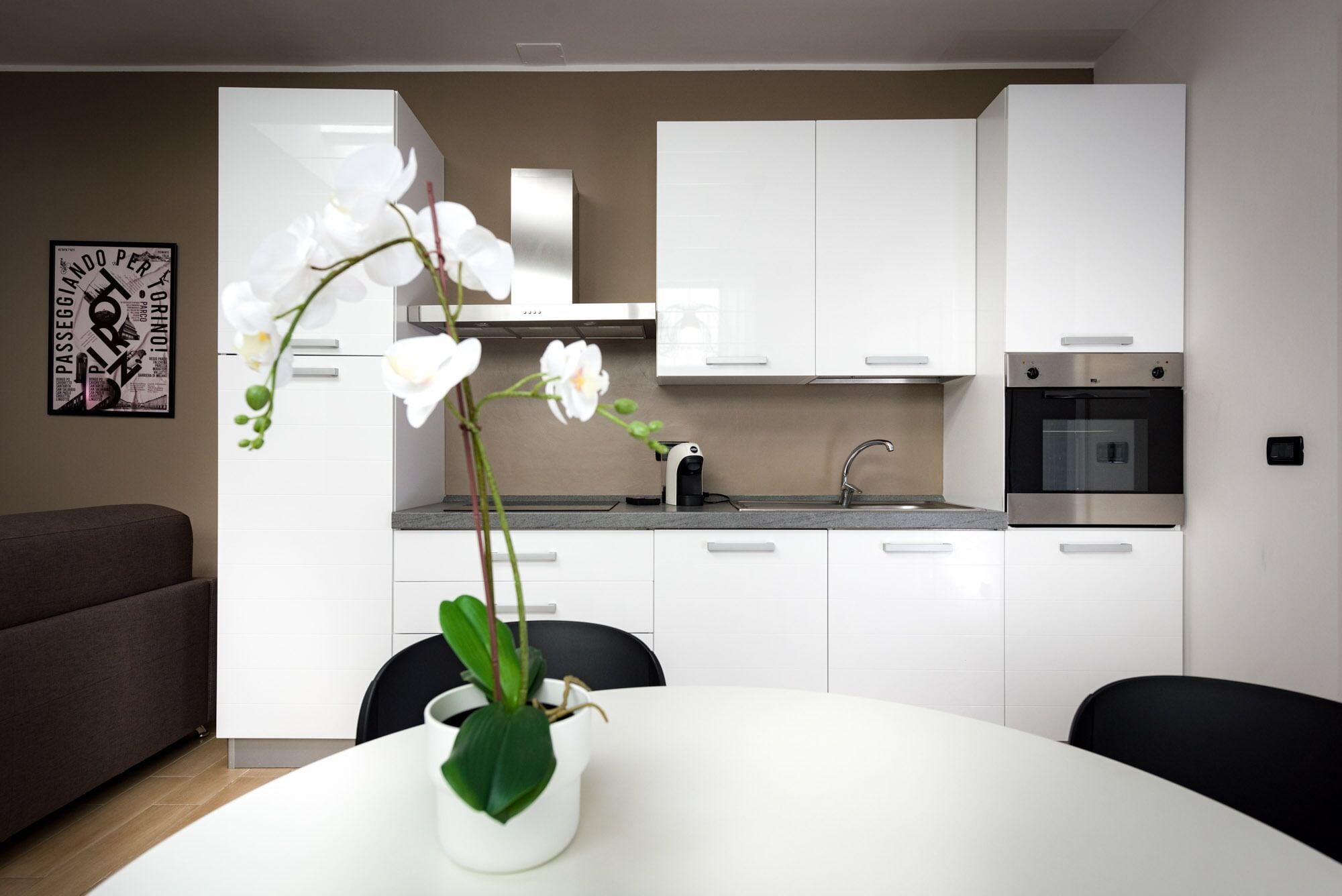 Une cuisine moderne avec des meubles blancs, un four en acier inoxydable et une machine à café posée sur le plan de travail.