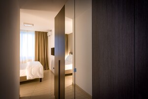 Una habitación de hotel con una cama, una mesita de noche, un espejo y una ventana con cortinas.