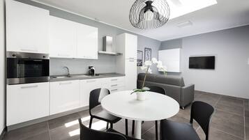 Une cuisine moderne avec des armoires blanches, un four encastré et un évier. On y trouve un coin repas avec une table ronde et des chaises, ainsi qu'un canapé gris.