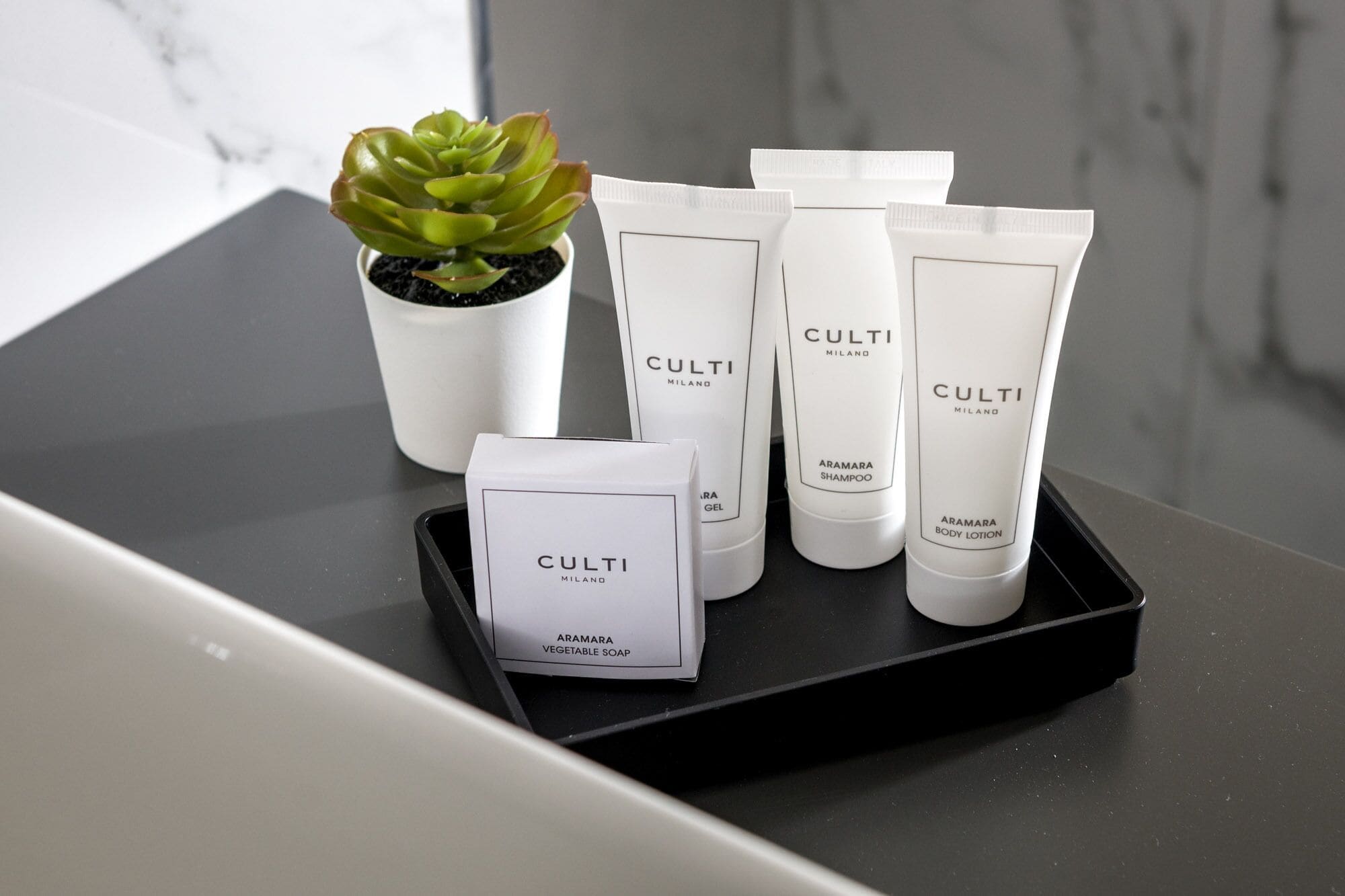 Ein Tablett mit verschiedenen Produkten von Culti Milano, darunter Körperlotion, Shampoo und Seife, neben einem Topf mit einer Sukkulente.