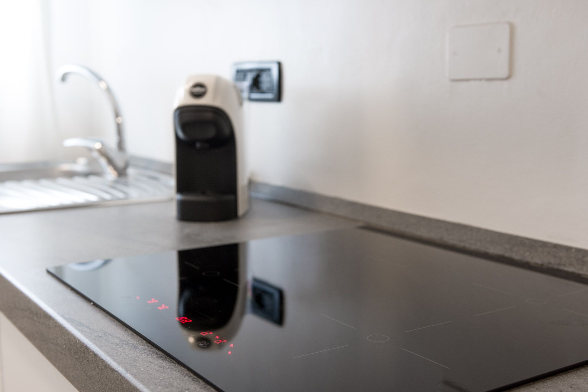 A modern kitchen with a black induction cooktop, a faucet, and a wall-mounted light switch.