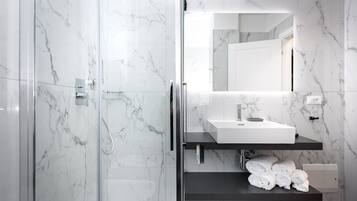 Ein modernes Badezimmer mit einer gläsernen Duschkabine, einem weißen Waschbecken und einem Handtuchhalter mit ordentlich gefalteten Handtüchern.