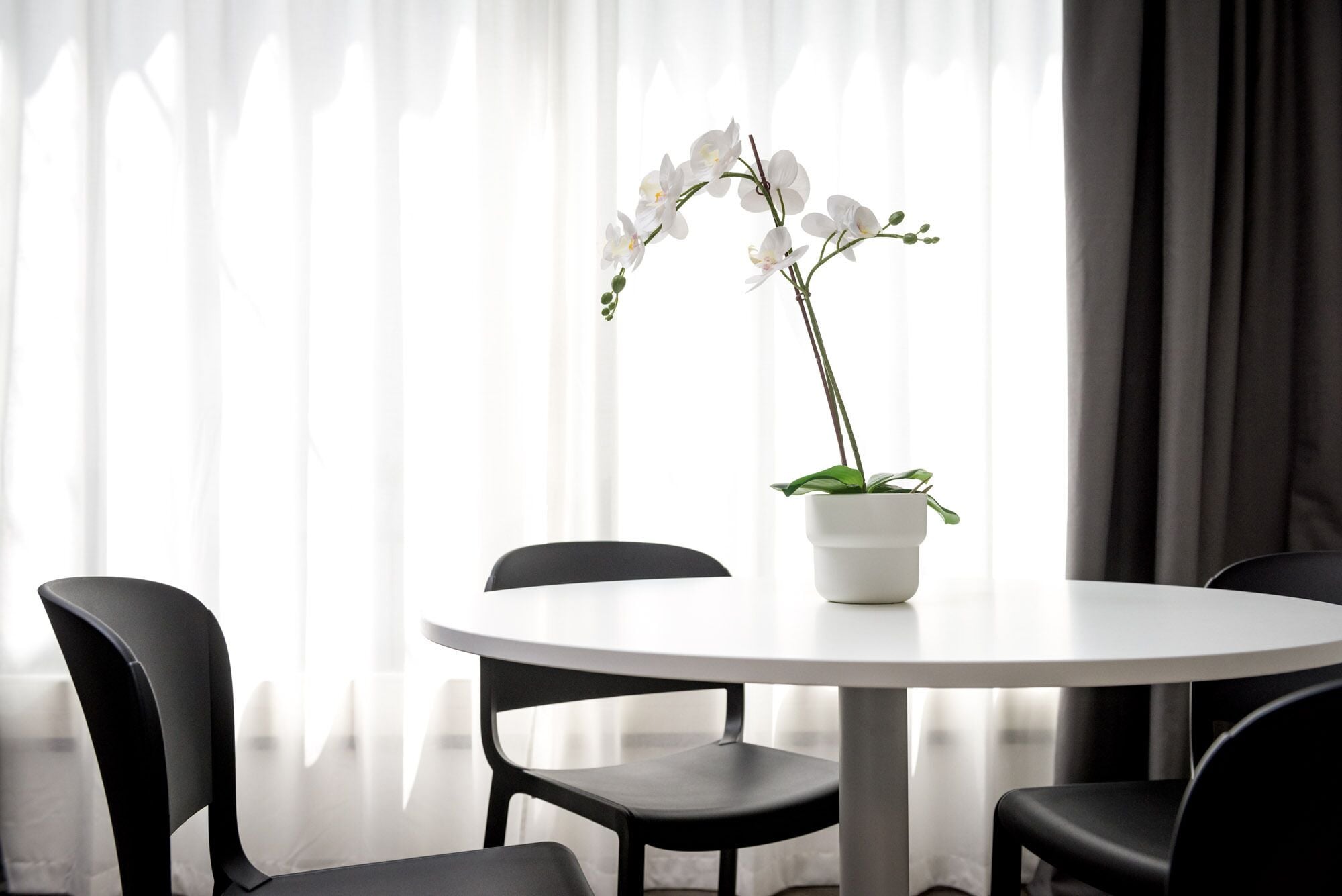 Une table ronde ornée d’une orchidée en pot au centre, entourée de chaises noires.