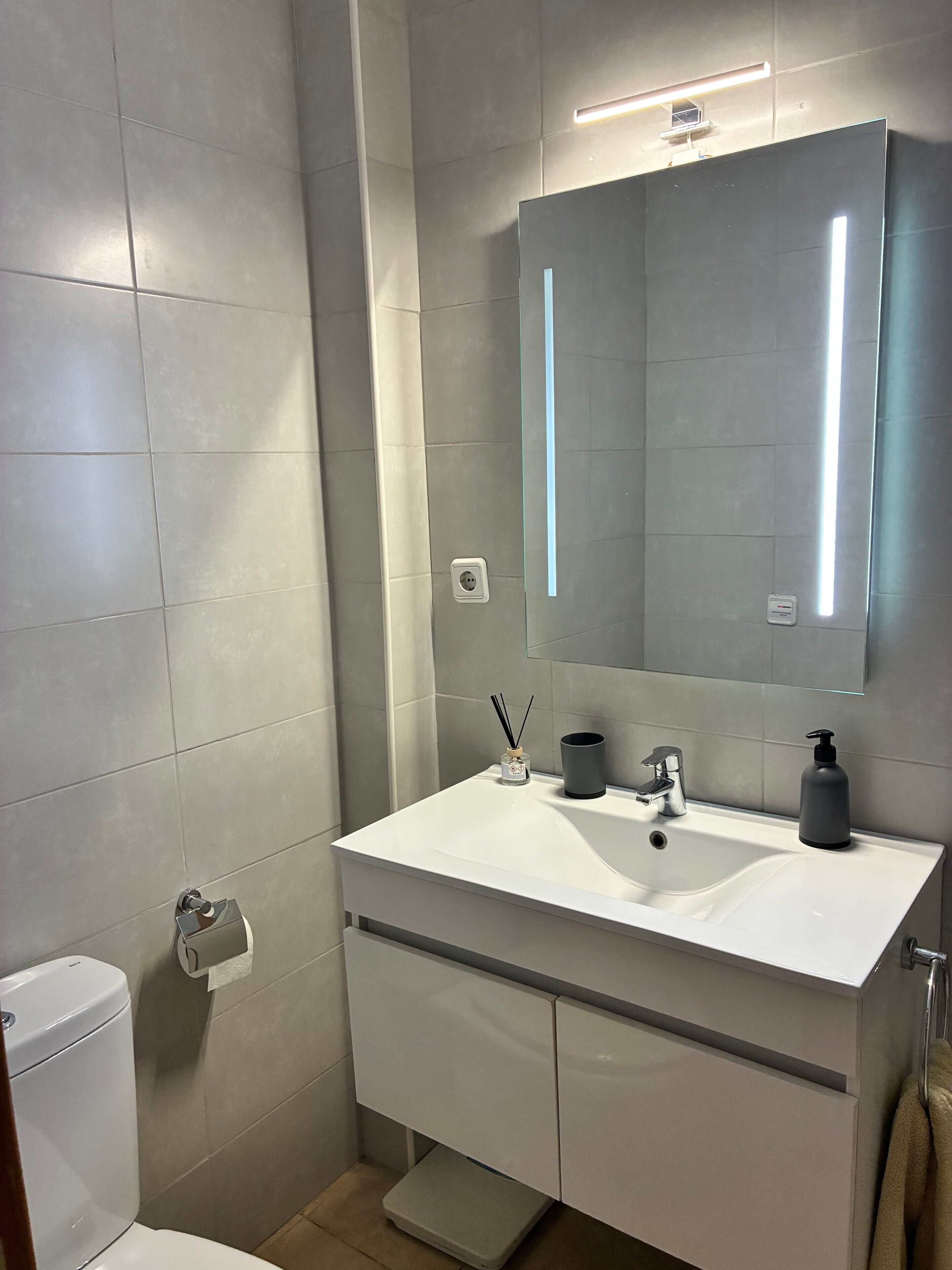 Un baño moderno con lavamanos, espejo e inodoro blancos.