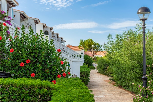 Un sentier bordé d’une végétation luxuriante et un bâtiment blanc coiffé d’un toit en tuiles.