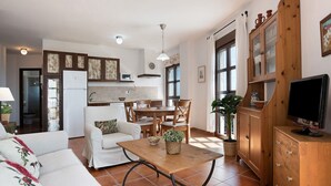 Eine moderne Küche mit Essbereich, weißen Möbeln und einem Fernseher auf einer Holzkommode.