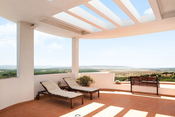 A terrace with two lounge chairs, a bench, and a potted plant.