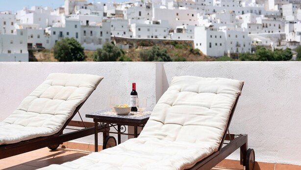 Ein Balkon mit zwei Liegestühlen, einem Tisch mit einer Weinflasche und einer Obstschale.