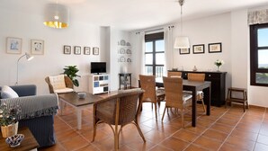 Un soggiorno con divano, poltrone, tavolo da pranzo, televisione e angolo cottura con finestra.