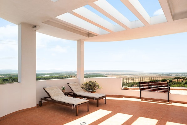 A terrace with two lounge chairs, a bench, and a potted plant.