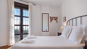 A hotel room with a large bed, a window with curtains, a bedside table with a lamp, and a wall-mounted mirror. - Apartment Cobijadas75 Segur with Mountain View, Balcony & Wi-Fi (Vejer de la Frontera)