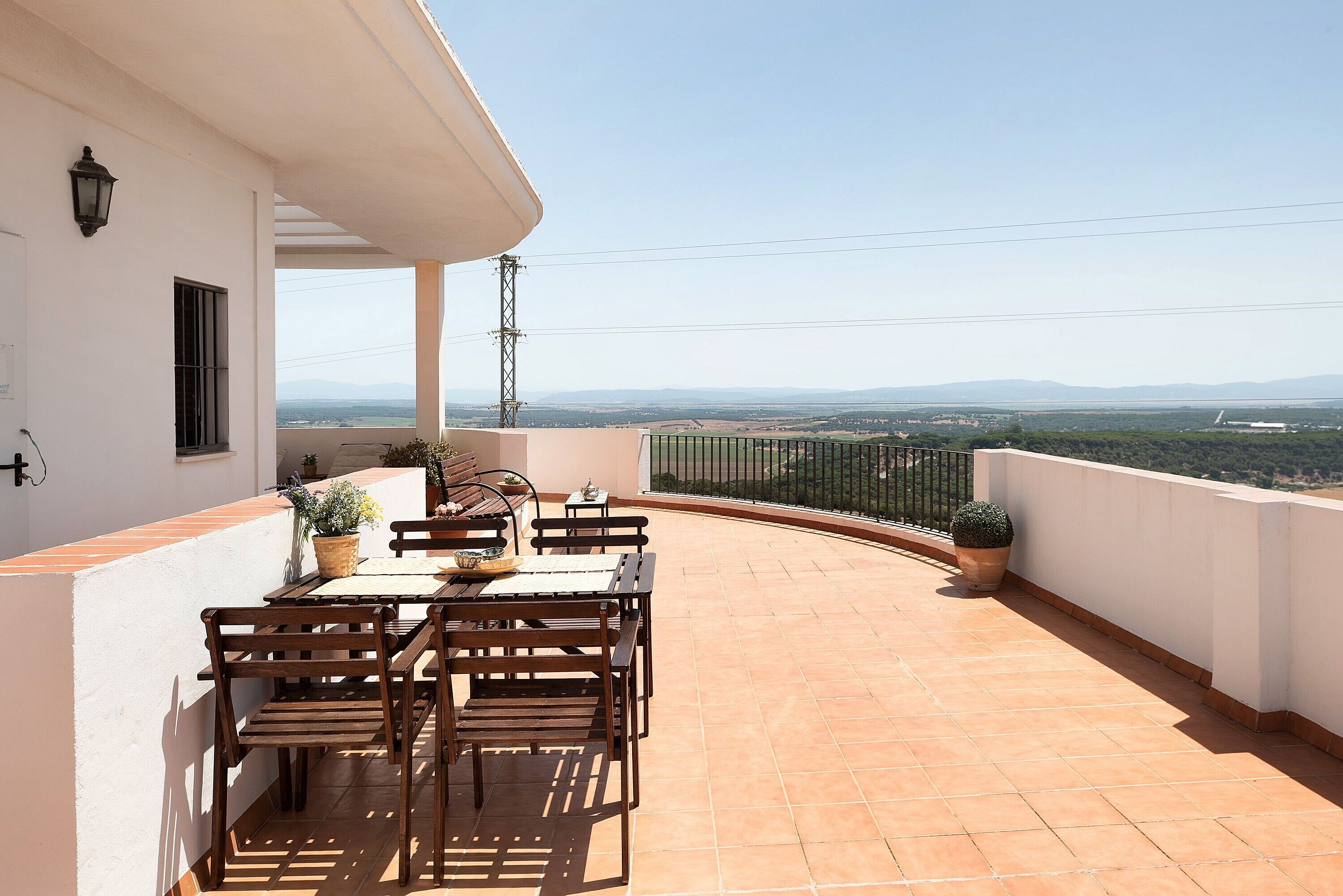 A terrace with a table and chairs, a potted plant, and a view of distant mountains.