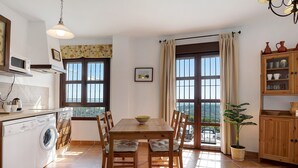 A kitchen with a washing machine, a dining table with chairs, a potted plant, and a view through the window. - Apartment Cobijadas75 Segur with Mountain View, Balcony & Wi-Fi (Vejer de la Frontera)