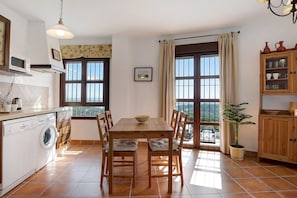 Une cuisine équipée d’un lave-linge, d’une table à manger avec des chaises, d’une plante en pot et d’une vue par la fenêtre.