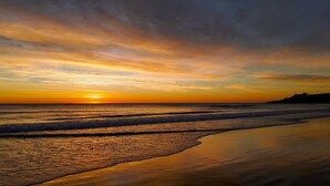 Une plage avec des vagues, un coucher de soleil et une côte lointaine.
