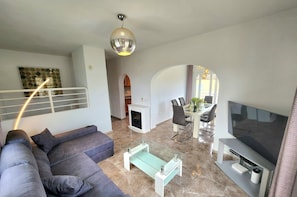 A modern living room with a sofa, a glass coffee table, a flat-screen TV, and a dining area with chairs and a table.