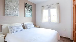 A bedroom with a large bed, two bedside tables, a window with curtains, and two wall art pieces.