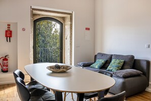 Une pièce comprenant une table à manger, des chaises, un canapé avec des coussins, un extincteur et une fenêtre donnant sur des arbres.