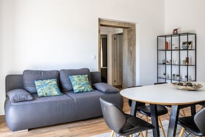 Un salon moderne avec un canapé gris, des fauteuils noirs, une table ronde et une étagère noire agrémentée d’objets décoratifs.