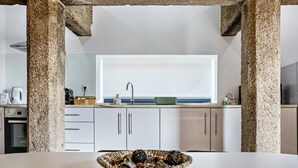 A modern kitchen with a large window, white cabinets, and a stone pillar. - Holiday Apartment 'Casa do Mestre T2' with Mountain View, Pool and Wi-Fi (Vila de Punhe)