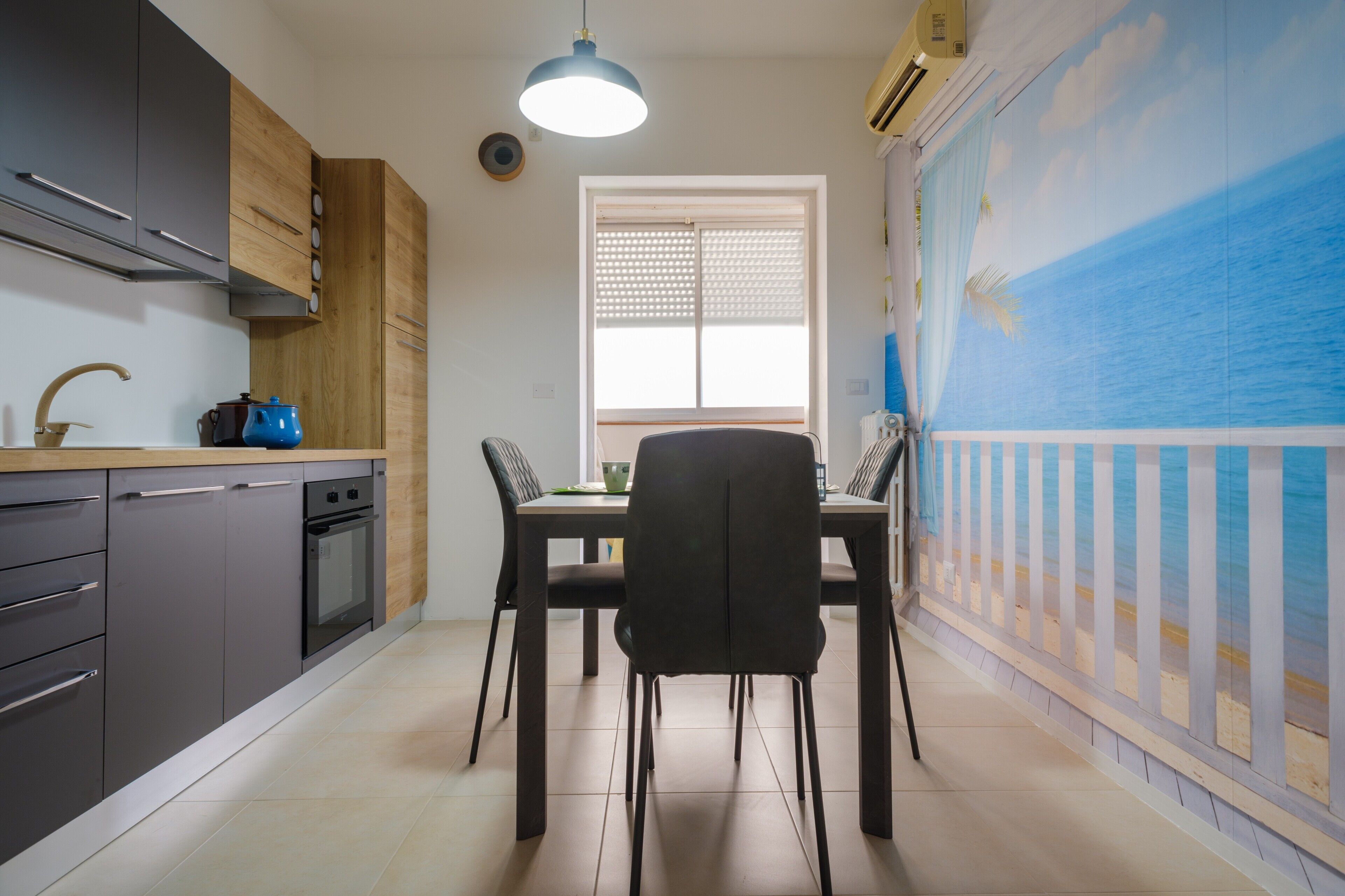 Une cuisine équipée d’appareils électroménagers modernes, une table à manger avec des chaises et une vue sur la mer par une fenêtre.