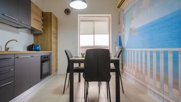 Une cuisine équipée d’appareils électroménagers modernes, une table à manger avec des chaises et une vue sur la mer par une fenêtre.