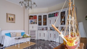 Un salon avec un canapé blanc, une table basse en bois, une maquette de bateau et un lustre.