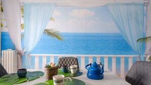 Un balcon avec vue sur l’océan, une table dressée avec une théière, des tasses et un panier.