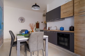 Une cuisine moderne avec des meubles de couleur sombre, un four encastré et un coin repas comprenant une table et des chaises.
