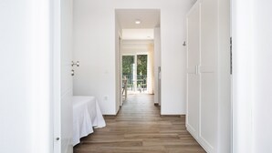 Un corridoio con pavimento in legno, pareti bianche e una porta che dà su un balcone con vista sul verde.