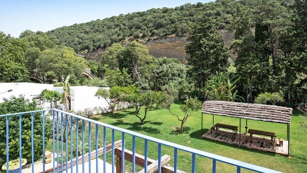Un balcone con vista su una zona verde, una panchina di legno e un pergolato.
