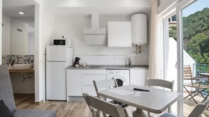A modern kitchen with white cabinets, a microwave, and a dishwasher. There is a dining area with a table and chairs, and a view of a balcony with outdoor furniture.