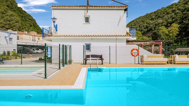 A swimming pool area with a white building, a fenced deck, and a lifebuoy.