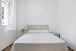 A bedroom with a bed, a nightstand, a window with curtains, and a wall-mounted light switch.