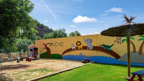 Ein Kinderspielbereich mit Wandgemälde, Picknicktisch und einem Strohdachschirm.