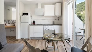 A modern kitchen with white cabinets, a microwave, and a dishwasher. There is a glass table with chairs in the foreground. - Apartment 'Casa de 10 - 5A' with Mountain View, Shared Pool & Wi-Fi (Vejer)