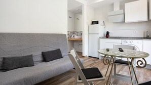 A modern living room with a grey sofa, a glass table with metal legs, and a kitchen area with white cabinets and appliances. - Apartment 'Casa de 10 - 5A' with Mountain View, Shared Pool & Wi-Fi (Vejer)