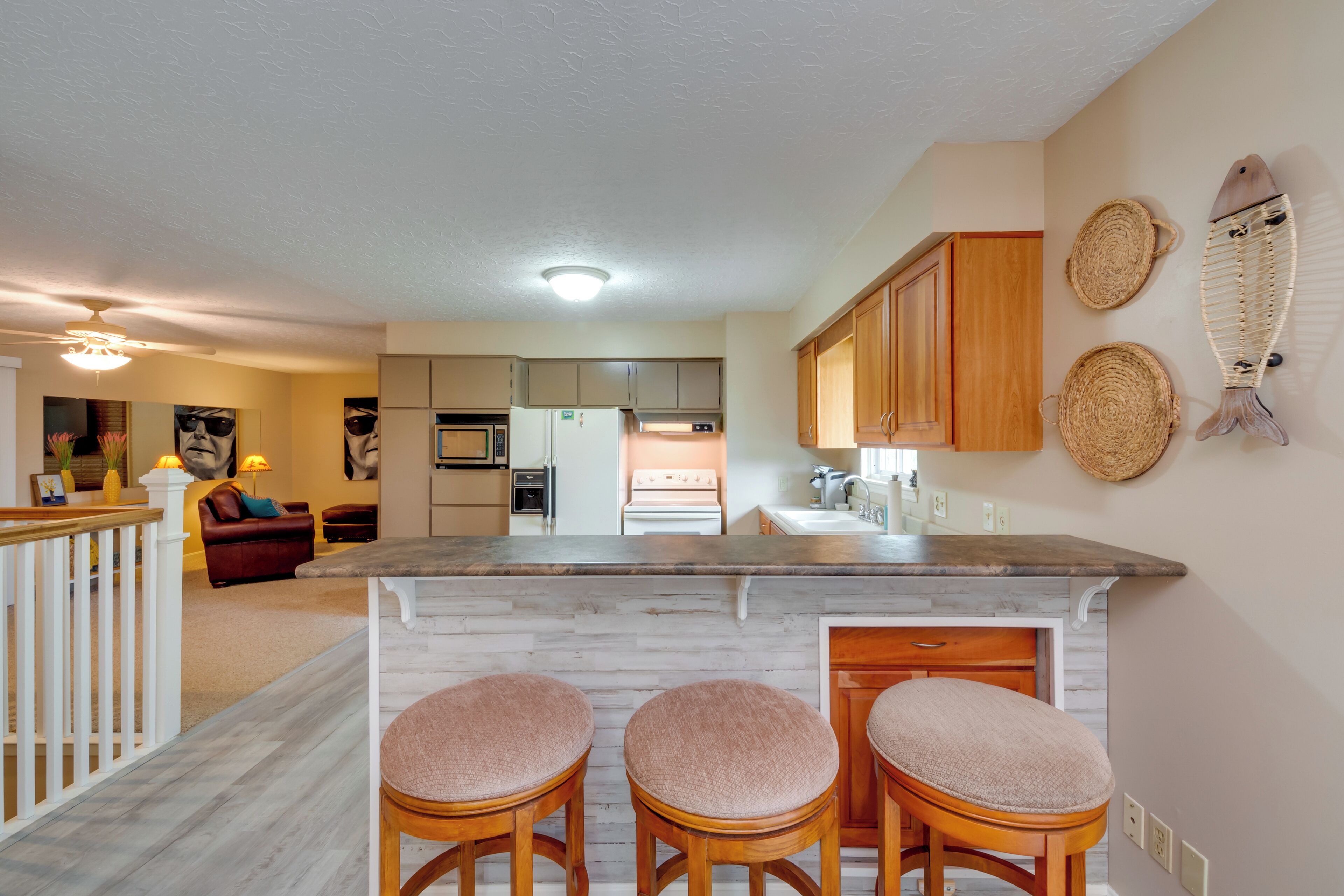 Una cucina moderna con isola centrale, sgabelli da bar in legno e cesti decorativi intrecciati appesi al muro.