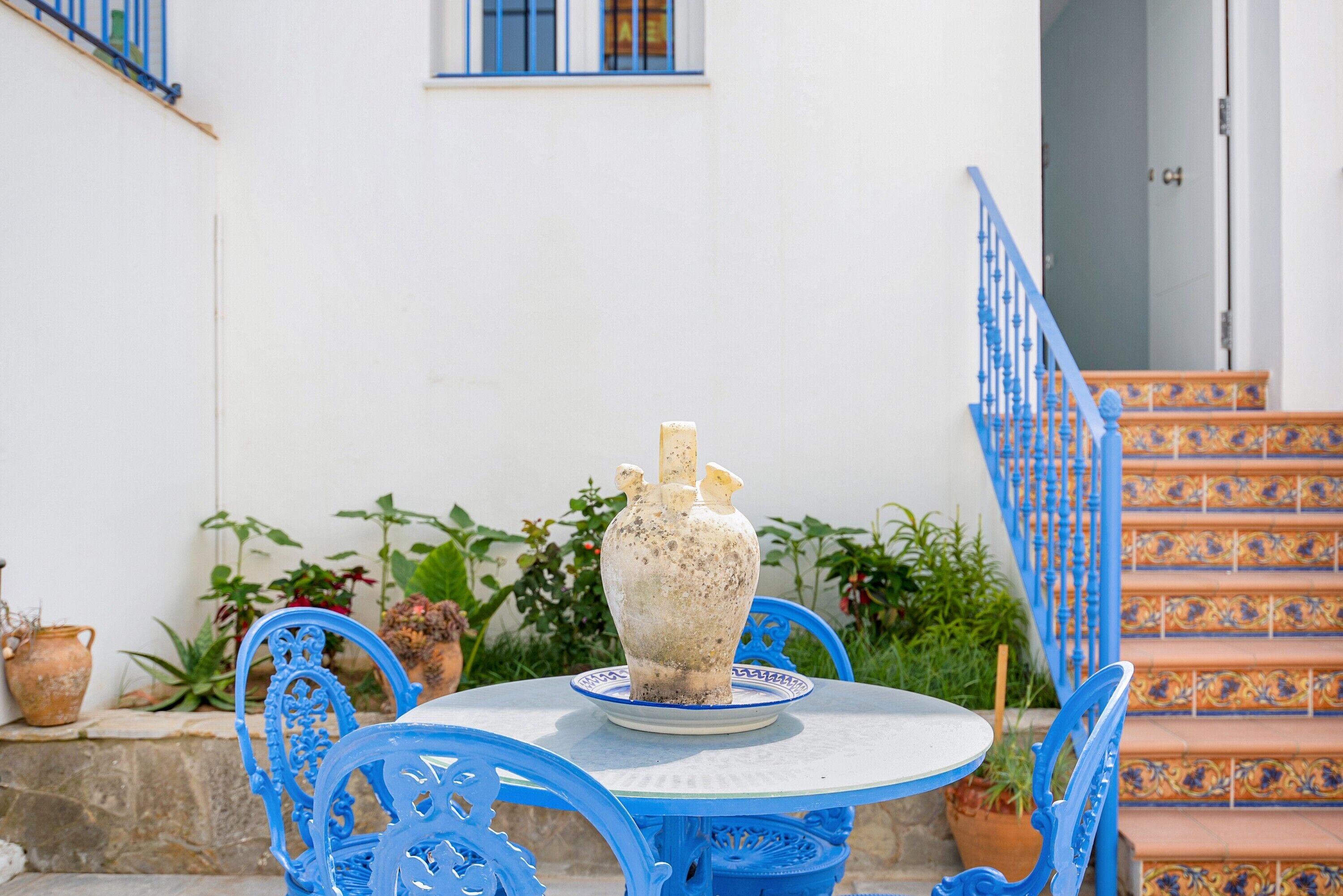A white wall with a blue door, a blue staircase, and a round table with a vase.