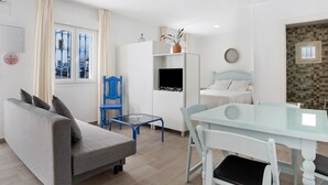 A modern living room with a sofa, a glass table, a TV, and a bed.