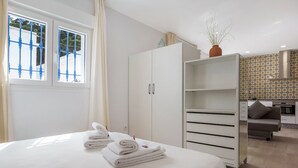 Habitación de hotel con cama, armario, pequeña kitchenette y vistas a través de una ventana con reja de metal.