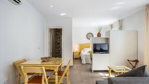 Un espacio habitable compacto con comedor, una kitchenette pequeña, cama y televisor.
