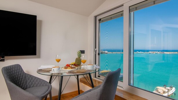 A modern room with a glass table, two grey chairs, a flat-screen TV, and a breakfast setup with fruit and drinks. - Seaview Modern Loft - Seaview Modern Loft (Zakynthos)